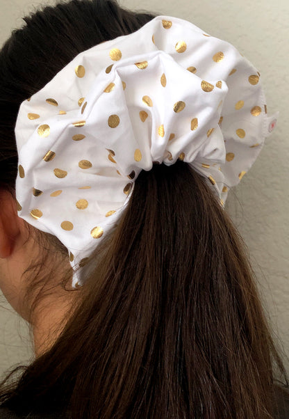 A model wearing the Golden Dazzle Oversized Scrunchie - a luxurious hair accessory featuring metallic gold polka dots on a bright white background, adding glamour and sophistication to any hairstyle